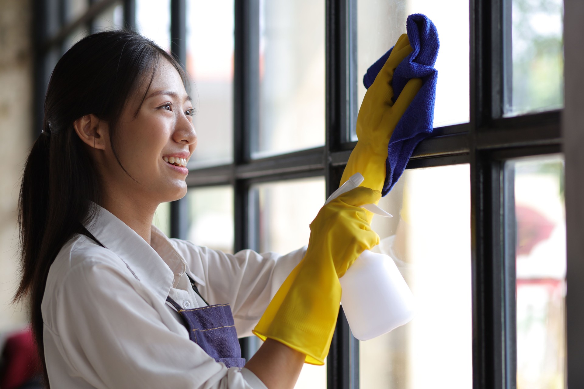 Person cleaning the room, cleaning staff is using cloth and spraying disinfectant to wipe the glass in the company office room. Cleaning staff. Maintaining cleanliness.